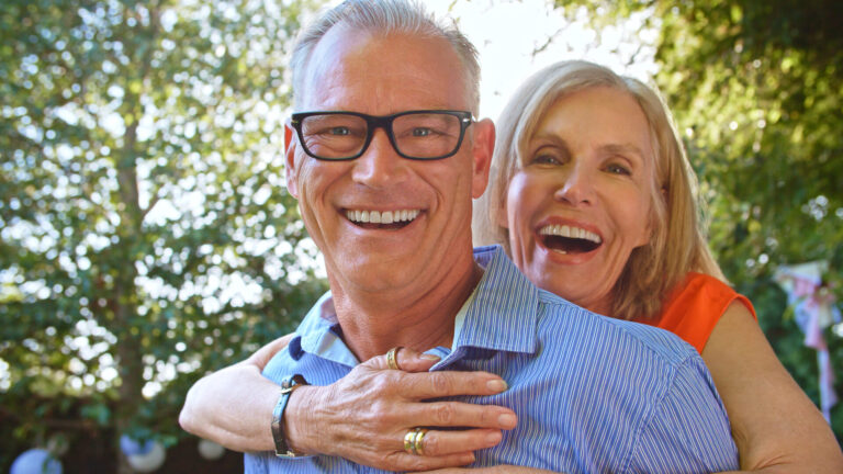 Outdoor Portrait Of Mature Couple With Woman Hugging Man From Behind With Lens Flare All-On-X Image